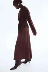 Top de manga larga color bordó, confeccionado en punto suave, con escote redondo y hombros caídos. Presenta un detalle de nudo y tiras laterales en la cintura.