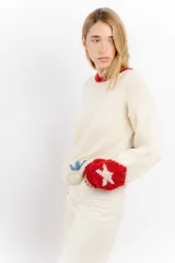 Sweater tejido a mano en lana merino color crudo, con cuello y puños en rojo. Presenta un diseño con motivos de un cowboy y estrellas.