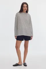 Remera manga larga de corte holgado, con diseño a rayas horizontales en tono blanco y negro, escote bote, pequeño bordado celeste en el pecho y estampa en la manga.
