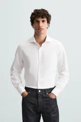 Camisa blanca de manga larga con cuello italiano abierto y cierre frontal de botonadura.