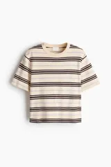Remera de punto tupido en color beige, con diseño a rayas horizontales en tonos marrón y lila. Presenta cuello redondo acanalado, mangas cortas con hombros caídos y bajo recto.