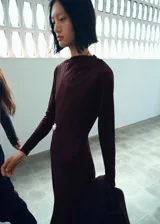 Vestido midi de corte evasé color marrón, confeccionado en tejido elástico, con cuello asimétrico y manga larga.