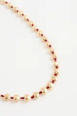 Collar largo con cuentas en forma de corazón color dorado, ensartadas en un cordón rojo.