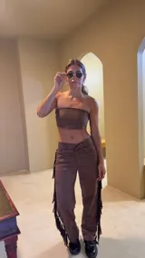 Pantalón marrón de gamuza con flecos laterales y ajuste con cordones en la cintura.