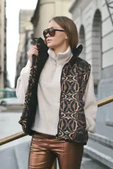 Chaleco marrón con estampado abstracto en tonos marrones y negros, con cierre frontal y broches a presión. Interior forrado con tela de peluche color crema y bolsillo interno.