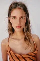 Vestido midi de color naranja con rayas diagonales marrones, escote fluido y tirantes finos cruzados en la espalda con abalorios. Presenta corte evasé con abertura frontal y forro interior.
