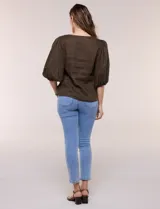 Blusa color beige confeccionada en lino, con escote en V pronunciado y cierre frontal de múltiples lazos para atar. Presenta mangas abullonadas tres cuartos con puños elásticos y corte relajado.