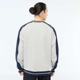 Buzo de felpa gris con cuello en V, detalles en azul marino y ribetes rayados en el cuello, puños y ruedo. Tiene corte holgado y mangas largas con paneles en contraste.