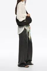 Bolso tipo media luna de nylon negro, con correa ajustable para llevar al hombro o cruzado. Presenta costuras verticales que le dan estructura y un pequeño logo de Bimba y Lola en la parte inferior central.