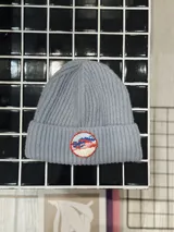 Gorro de lana celeste con diseño de punto acanalado y parche circular bordado con motivo de montañas y cielo.
