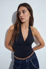Top halter negro de silueta ajustada y diseño cropped, con escote profundo en V y frunce bajo el busto. Presenta espalda descubierta con lazo regulable en el cuello.