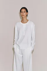 Camiseta blanca de manga larga y corte regular fit, confeccionada en mezcla de algodón y lino. Presenta cuello panadero con cierre frontal de botones y bajo recto.