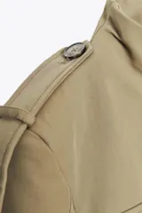 Chaqueta de estilo militar en color beige, con cuello subido, cierre frontal de botones, bolsillos de plastrón con solapa en el delantero y detalle de solapas en el pecho. Presenta mangas largas con hombreras y trabillas decorativas.