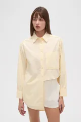 Camisa blanca de algodón, de corte holgado, con cuello camisero, botones frontales, un bolsillo de parche en el pecho y mangas largas con puños abotonados.