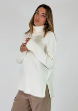 Sweater de cuello alto en color beige, con diseño de punto liso y terminaciones acanaladas en puños y ruedo. Presenta aberturas laterales en el bajo y un detalle de borde desflecado en el ruedo y los puños.