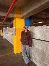Camisa de lino color marrón con cuello redondo decorado con volados, cierre frontal de botones y mangas largas con puños ajustados.