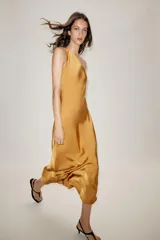 Vestido midi de satén color mostaza con escote asimétrico de un solo hombro y corte evasé. Presenta pliegues en el hombro y cierre lateral con cremallera oculta.