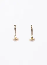Aros tipo huggies de plata 925 con baño de oro 18k, decorados con incrustaciones de zirconias y un colgante de perla de río.