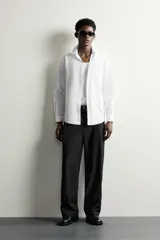Camisa de vestir blanca de corte slim fit, confeccionada en tejido de algodón con textura estructurada. Cuenta con cuello italiano, mangas largas con puños abotonados y cierre frontal con botonadura.