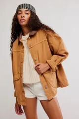 Campera oversize de denim en color marrón, con hombro caído, cuello de lona marrón en contraste, bolsillos frontales con solapa, cierre de botones metálicos y puños abotonados.