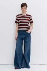 Remera de manga corta con diseño a rayas horizontales en tonos bordó, blanco y celeste. Presenta cuello redondo y un pequeño parche circular con logo en el pecho.