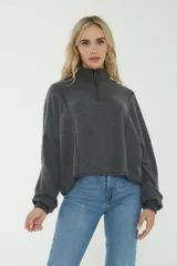 Buzo gris oscuro de punto con cuello alto y cierre frontal parcial. Cuenta con mangas largas y diseño holgado con costuras decorativas verticales.