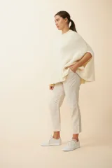 Poncho color crema de tejido de punto industrial con cuello alto y aberturas laterales para los brazos.