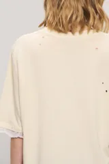 Remera oversize de jersey de algodón en color blanco, con cuello redondo, mangas cortas y largo a la cadera. Presenta estampa frontal con la inscripción "Gypsy Lover", detalles de roturas y apliques de puntilla en las mangas y el ruedo.