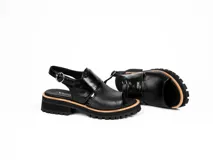 Sandalia de cuero vacuno color negro con diseño de punta abierta y talón descubierto. Presenta una tira ancha sobre el empeine en cuero charolado y una tira ajustable con hebilla metálica en el tobillo. Cuenta con una suela de goma tipo track con plataforma bicolor.