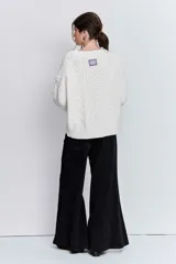 Sweater de punto color blanco off-white, con cuello redondo y diseño texturizado con trenzas y pompones en el frente.