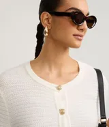 Cardigan de punto texturizado color blanco, con cuello redondo, manga larga y cierre frontal de botones metalizados dorados. Cuenta con dos bolsillos aplicados al frente y puños y dobladillo en rib.
