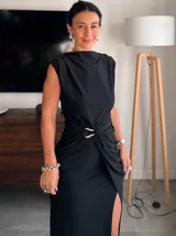 Vestido largo color beige, sin mangas, con escote redondo y detalle de frunces laterales en la cintura que crean un efecto drapeado y una abertura frontal en la falda.