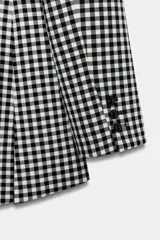 Blazer Zara Woman Collection de corte asimétrico con estampado de cuadros vichy en blanco y negro. Presenta cuello solapa, cierre frontal con botones y un diseño de bajo irregular con abertura central.
