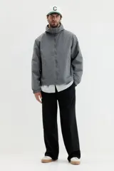 Campera rompevientos de nylon color gris oscuro, con forro de malla. Presenta cierre frontal con protección para el mentón, capucha ajustable con cordón, bolsillos laterales y un bolsillo interior, todos con cierre. Los puños y el bajo tienen elástico revestido.