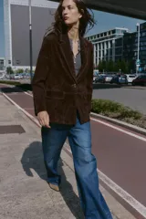 Blazer de piel 100% color marrón oscuro, con cuello solapa, manga larga con hombreras y bolsillos delanteros con solapa. Presenta pespuntes decorativos en contraste y cierre frontal con un botón.