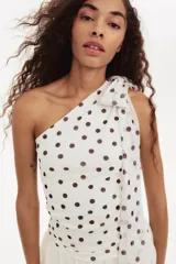 Top entallado de malla transparente color blanco con lunares negros. Presenta un escote asimétrico, un solo bretel y tiras anchas que se atan al cuello. Incluye forro de punto.
