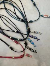 Collar con cordón ajustable de color y dije de pez esmaltado con detalles de piedras de colores.