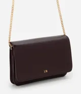 Cartera bandolera pequeña de poliuretano color marrón oscuro con acabado texturizado. Cuenta con solapa frontal, logo metálico dorado en la parte inferior y correa larga de cadena metálica dorada.