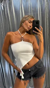 Top blanco estilo halter con escote strapless y detalle de argolla metálica en el cuello. El bajo es asimétrico y anudado.