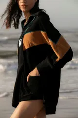 Hoodie de tela de toalla color azul, con cuello alto y cierre frontal de cremallera amarilla. Presenta bloques de color rojo en los hombros y detalles de ribetes amarillos. Tiene un bolsillo tipo canguro y un parche decorativo en el pecho.