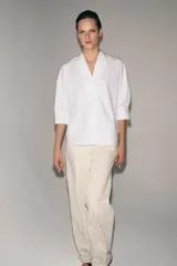 Camisa de algodón con cuello redondo y escote en pico, mangas tres cuartos con puños y bajo asimétrico redondeado.