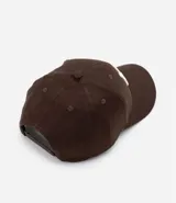Gorra de seis paneles con ala curva, confeccionada en algodón color marrón. Presenta un bordado frontal con las letras NY en color blanco y cuenta con cierre strapback ajustable en la parte posterior.