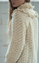 Cardigan tejido a crochet en lana merino color crudo, con volados dobles en hombros y cuello, canesú con tejido abierto y ajuste frontal con cuatro botones de guampa tallados a mano.