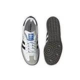 Championes Adidas modelo Samba OG, de diseño clásico con exterior de cuero blanco, tres tiras laterales negras, puntera de gamuza gris y suela de goma color marrón.