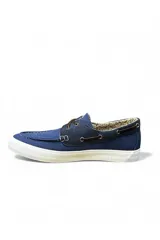 Zapatos náuticos de lona azul con cordones de cuero marrón, suela blanca y detalles de costuras visibles.