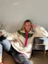 Canguro de polar color crema con bloques de color verde militar en la parte superior y fucsia en los bordes y cierre.