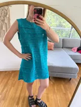 Vestido corto de algodón color turquesa, sin mangas y con cuello redondo. Presenta un tejido calado con diferentes patrones de punto.