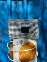 Necessaire con estampado a cuadros blanco y negro, grifa de goma, detalles de cordón, cierre y bolsillo transparente interior.