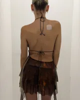 Vestido corto de color marrón con estampado tie-dye en tonos anaranjados. Presenta un escote halter profundo con tirantes finos y una falda corta con volados.