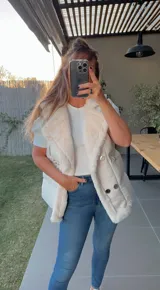 Chaleco puffer blanco con cuello de piel sintética y cierre con broches metálicos.